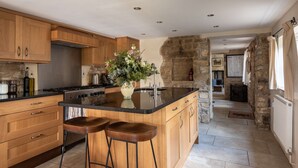 A modern kitchen with wooden cabinets, a black countertop, and a central island with stools. - Camside, Chipping Campden - Taswell Retreats (Chipping Campden)