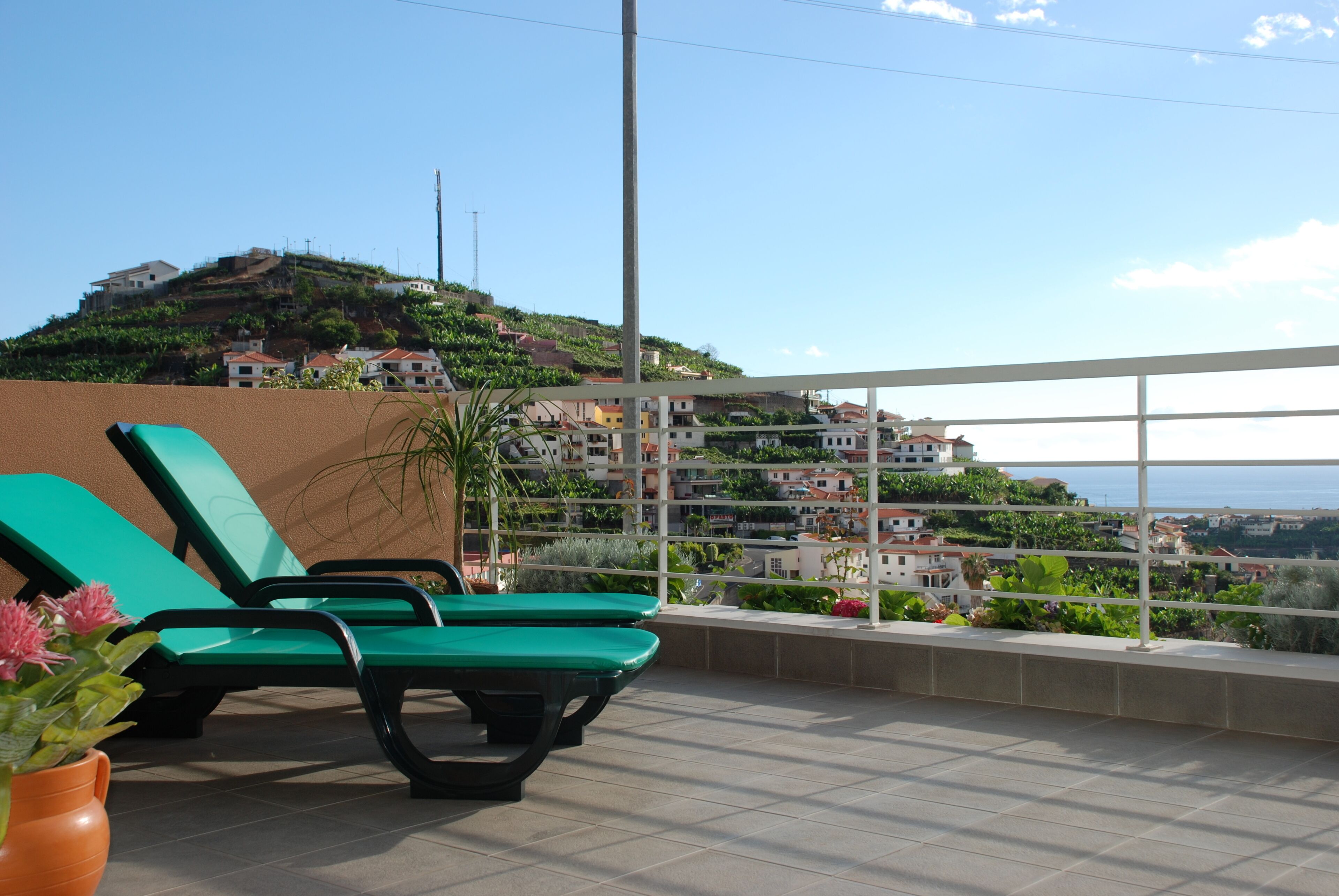 A terrace with green lounge chairs and a view of a hillside with buildings.