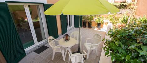 A patio with a table and chairs, a yellow umbrella, and potted plants.