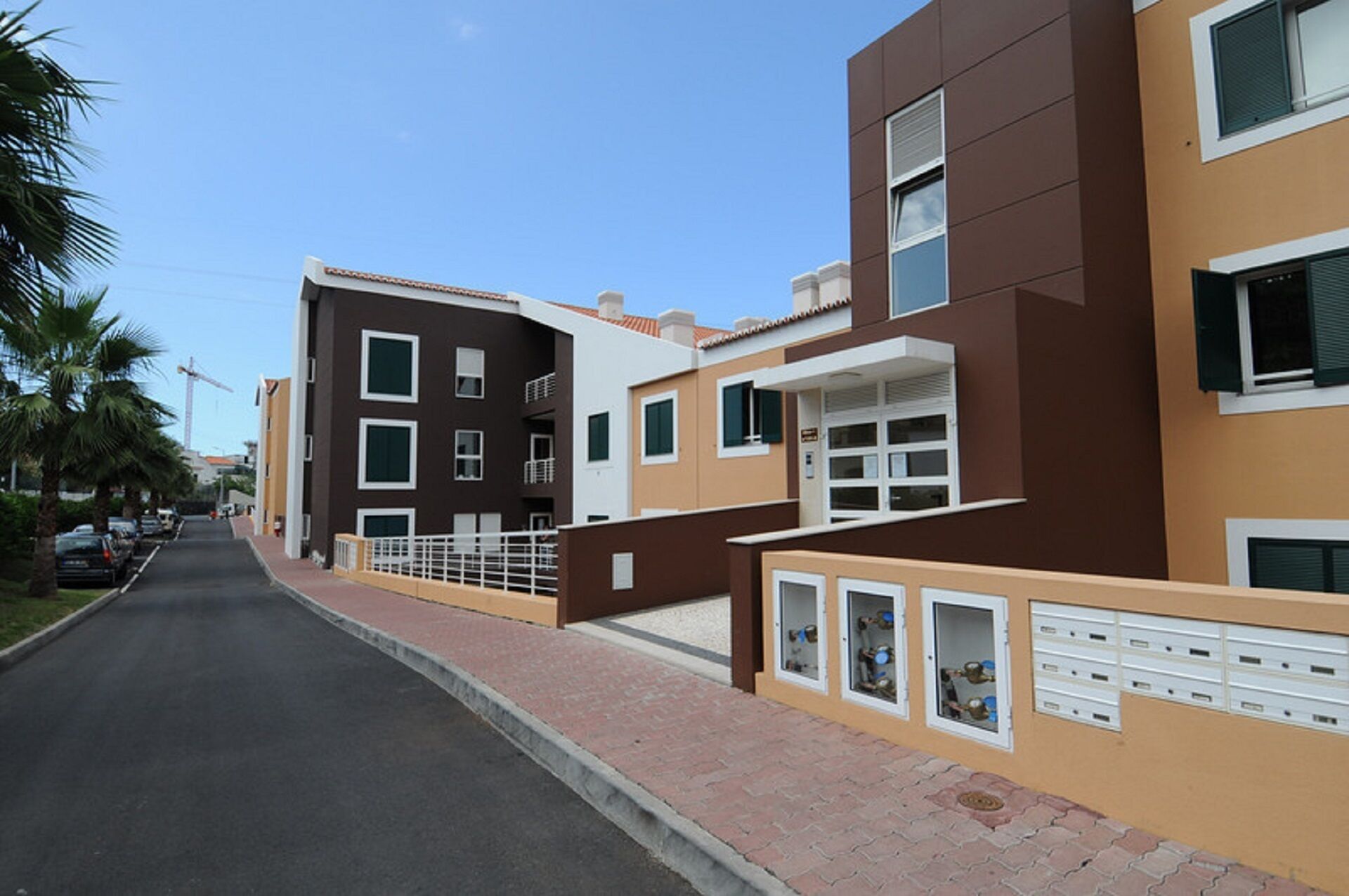 A modern residential building with a flat roof, multiple windows, and a gated entrance.