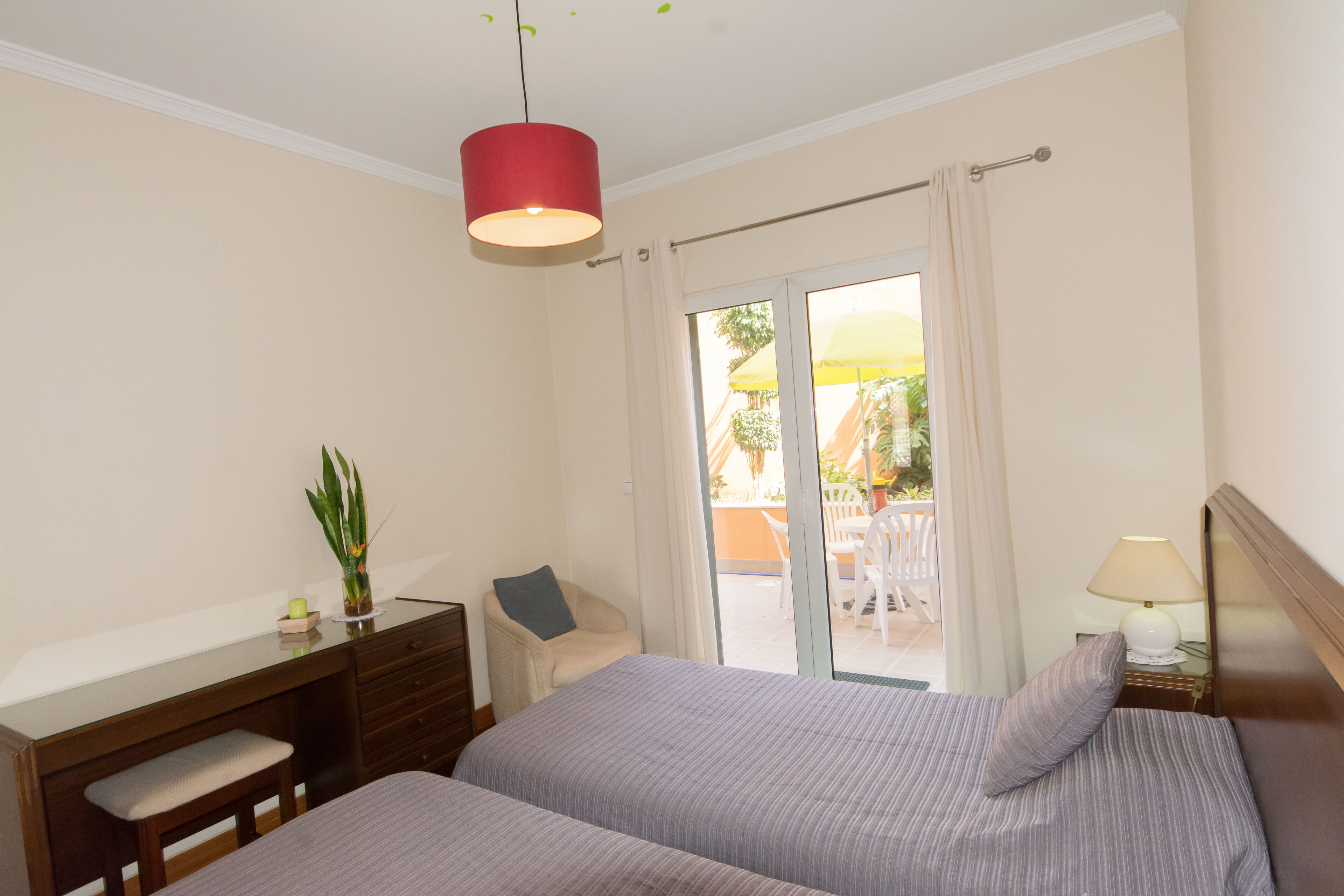 A hotel room with two beds, a desk, a chair, a lamp, and a view of the outside.