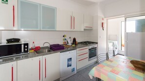 Een compacte keuken met witte kastjes, een magnetron, een vaatwasser en een fornuis.
