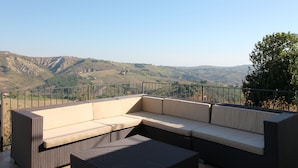 Un balcon avec un canapé en osier et une table à manger, offrant une vue sur un paysage montagneux.