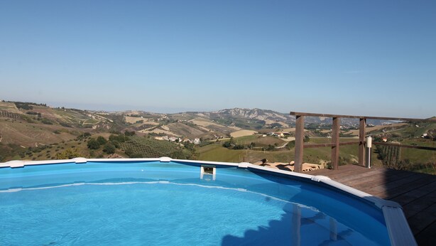 Une piscine avec une terrasse en bois et une vue sur des collines ondoyantes.