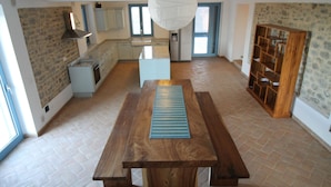 Une cuisine spacieuse avec un îlot central, un coin repas doté d’une table en bois et un mur en pierre.
