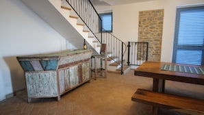 Un vaste espace de vie comprenant un banc en bois, un banc en bois rustique agrémenté de coussins, un escalier avec une rampe en métal et un mur d’accent en pierre.
