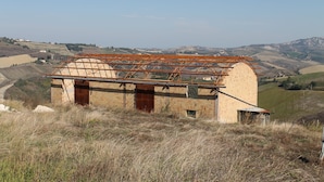 Un bâtiment rustique de plain-pied, doté d’un toit en métal et de murs en briques, situé sur une colline et offrant une vue panoramique sur des collines ondoyantes et des bâtiments éloignés.
