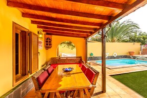 Una mesa de comedor de madera con cojines rojos, una piscina y un patio cubierto.