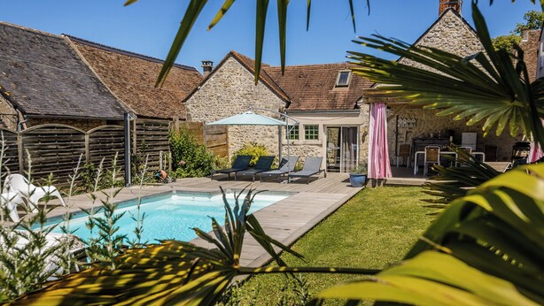 Ein Garten mit Swimmingpool, Liegestühlen und einem Steinhaus.