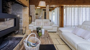 Ein gemütliches Wohnzimmer mit Kamin, weißen Sofas und einer Holzbalkendecke.