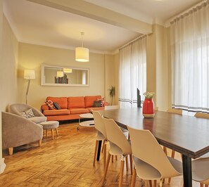 A modern living room with a sofa, chairs, a dining table, and a large window with curtains.