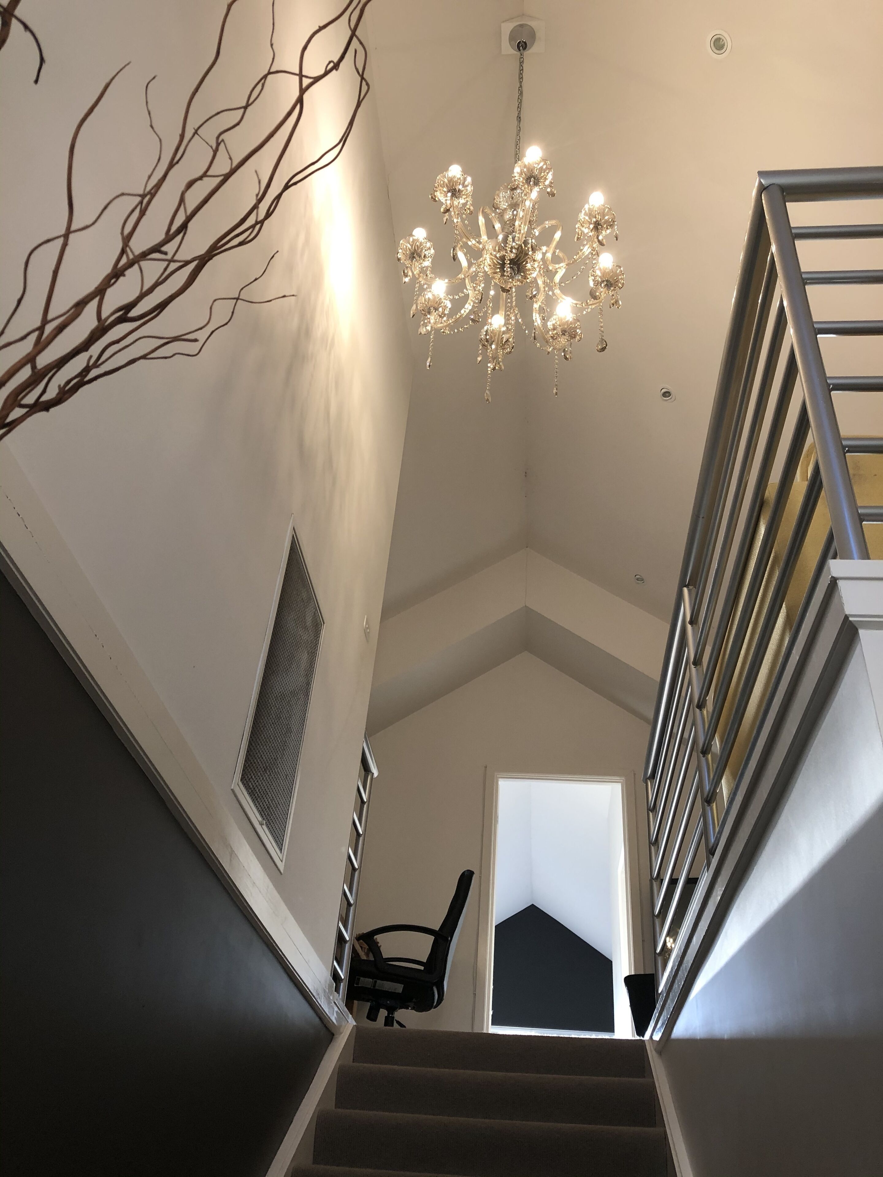 A staircase with a chandelier, a chair, and a door at the top.