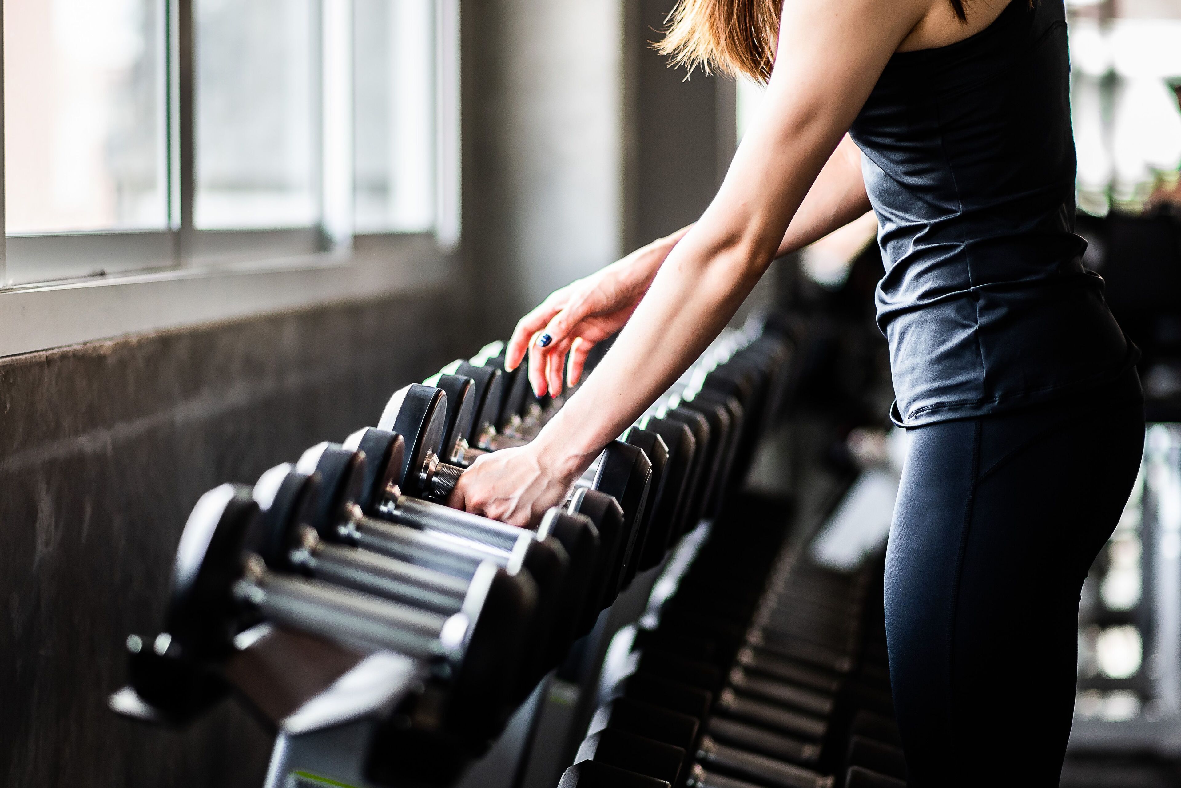 A person using a row of dumbbells in a gym with a window in the background.