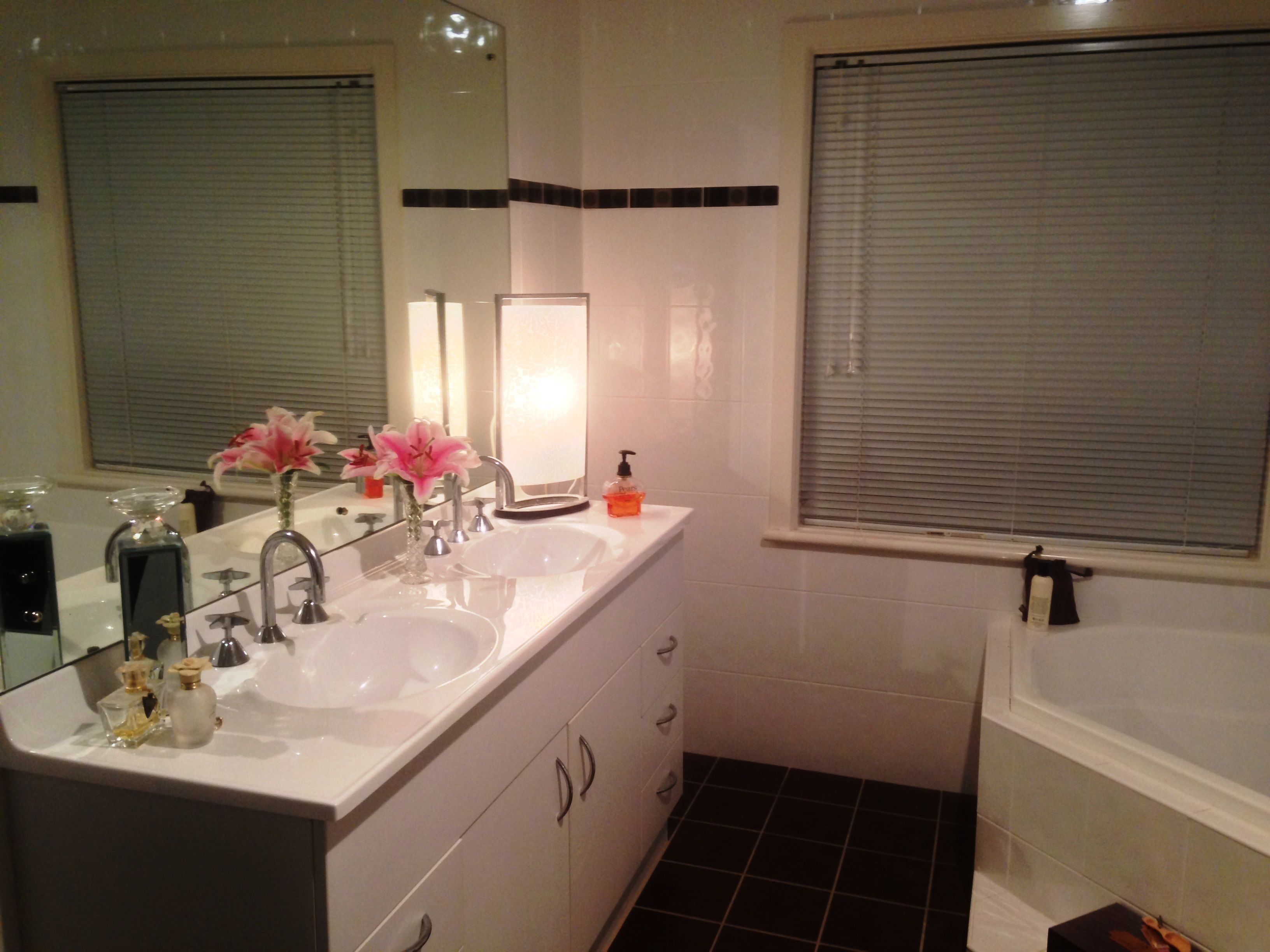 A bathroom with two sinks, a mirror, and a window with blinds.