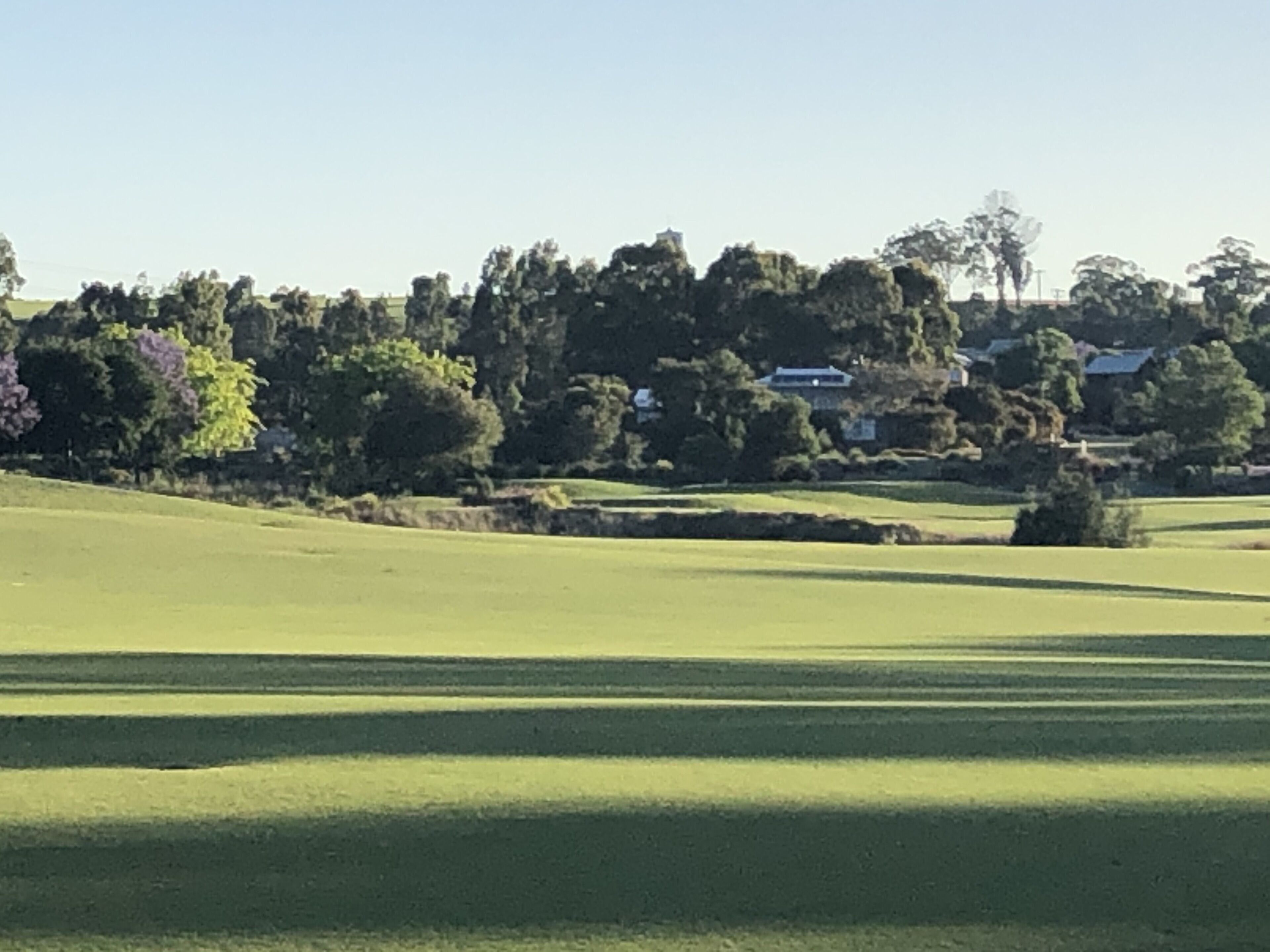 A golf course with a clear view of the fairway, sand bunkers, and a backdrop of trees and houses.