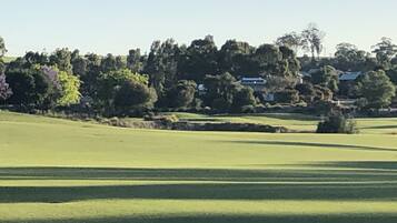 A golf course with a clear view of the fairway, sand bunkers, and a backdrop of trees and houses.