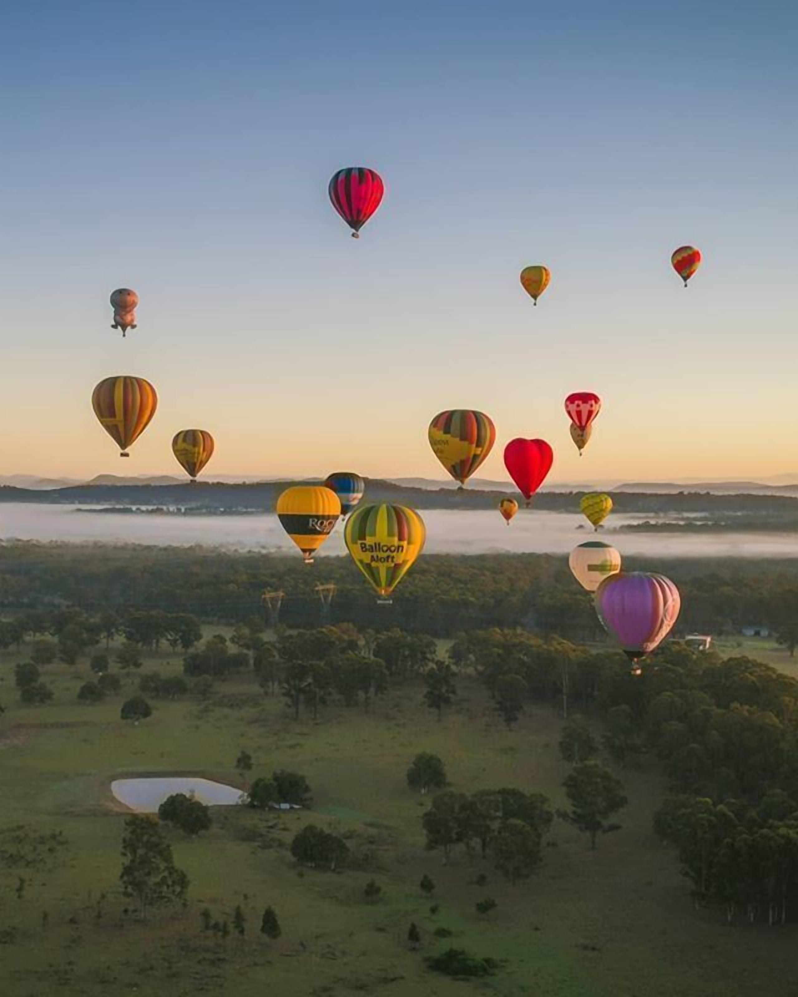 A landscape with multiple hot air balloons in the sky.
