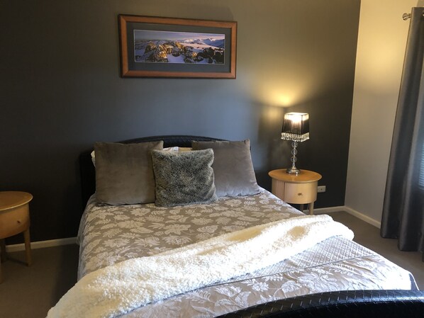 A neatly made bed with a patterned bedspread and pillows, a bedside table with a lamp, and a framed picture on the wall. - Gumnut Grove The Vintage (Pokolbin)