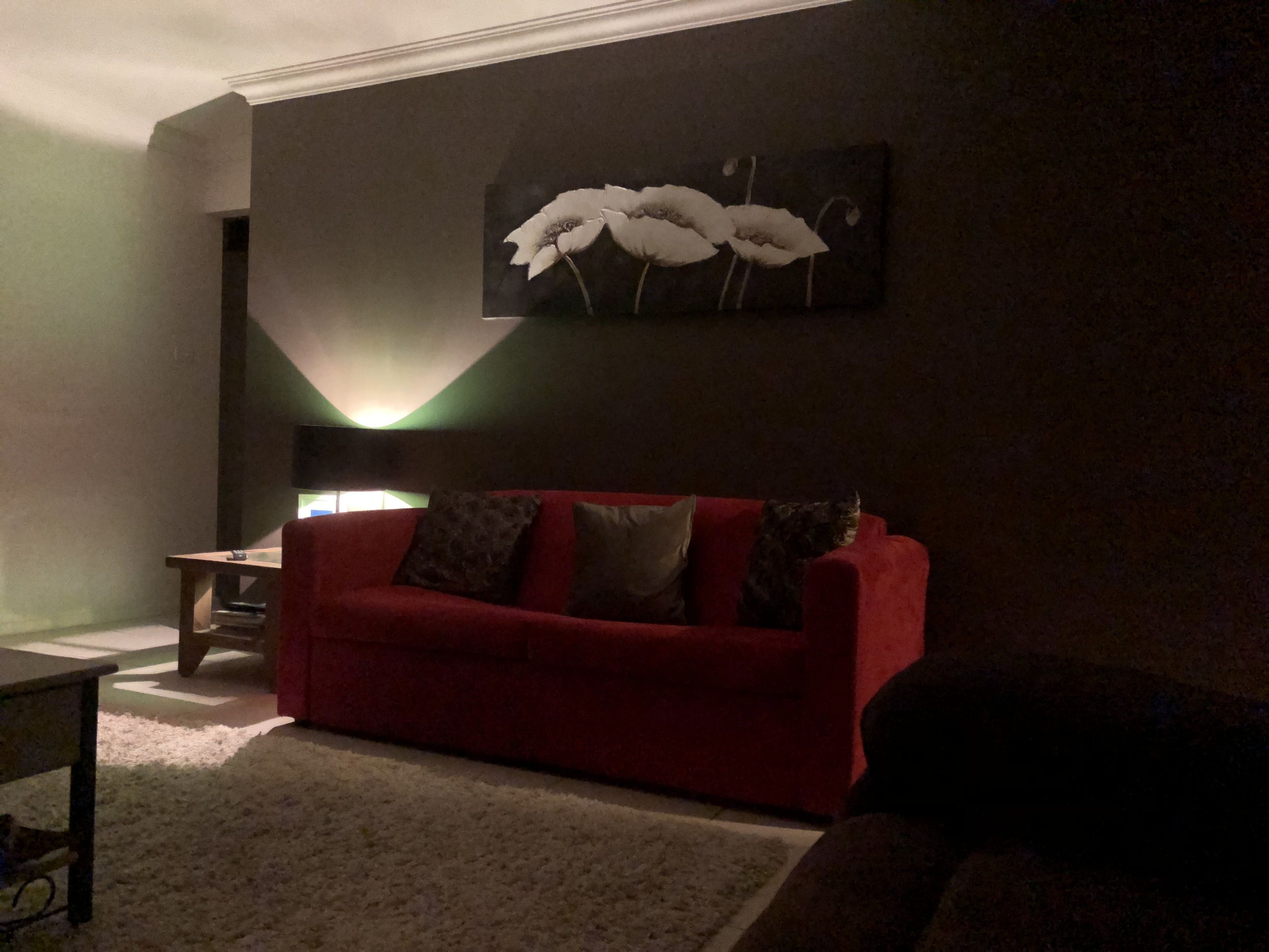 A living room with a red sofa, a small table, and a wall-mounted painting.