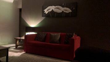 A living room with a red sofa, a small table, and a wall-mounted painting.