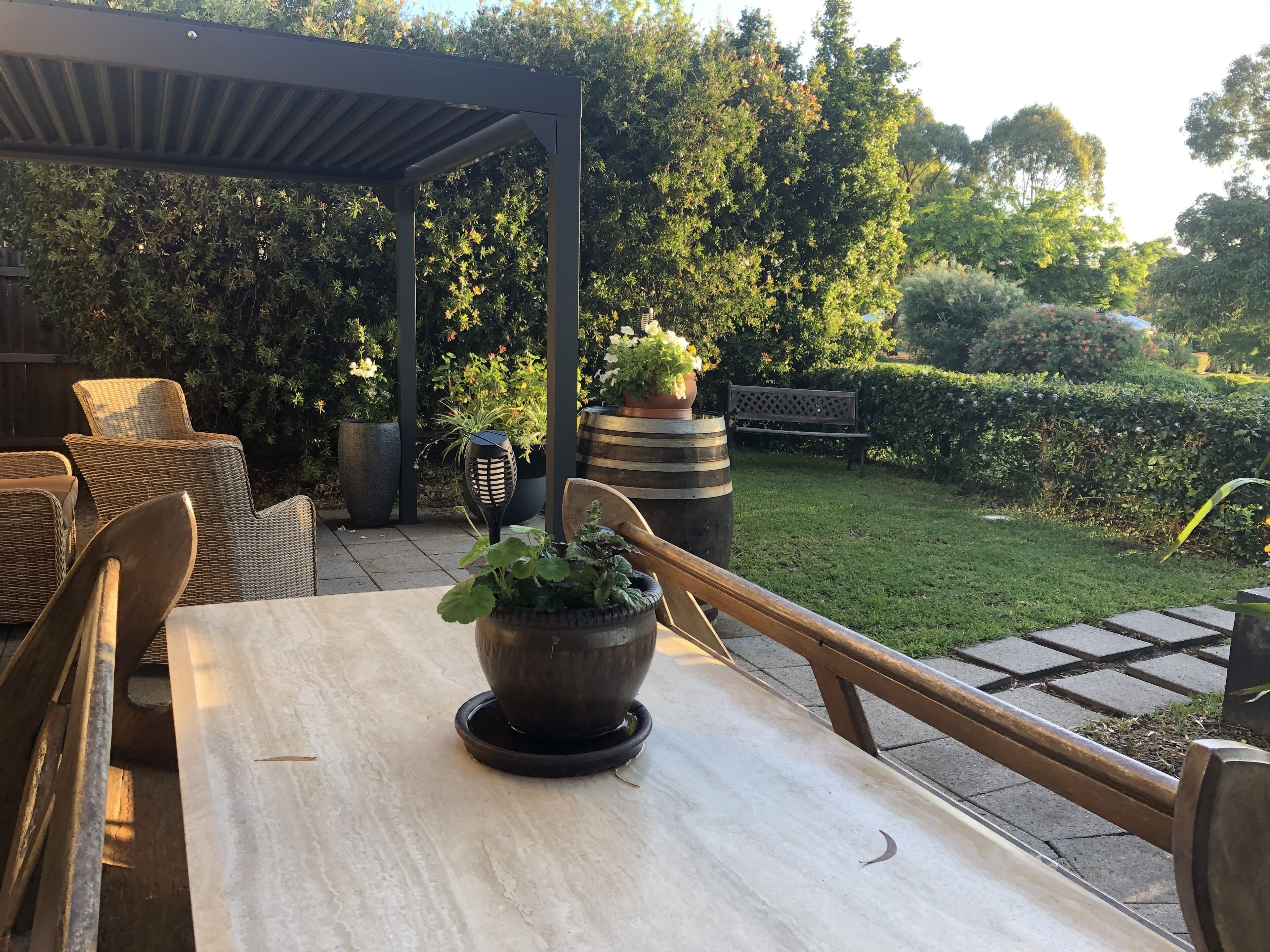 Un patio al aire libre con mobiliario de mimbre, una mesa con una planta en maceta y un jardín al fondo.