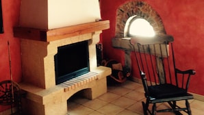 Une pièce avec une cheminée en pierre, une chaise en bois et un mur rouge.
