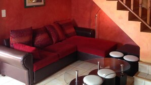 Un salon avec un canapé rouge, un escalier en bois et une œuvre d’art encadrée au mur.