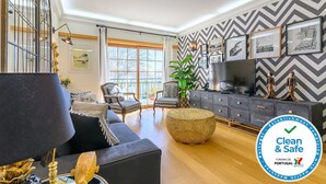 A modern living room with a sofa, armchair, and ottoman, a television, and a decorative plant. - CARCAVELOS BEACH. A wonderful 2 bedroom apartment (Carcavelos)