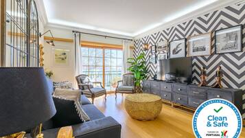 A modern living room with a sofa, armchair, and ottoman, a television, and a decorative plant.