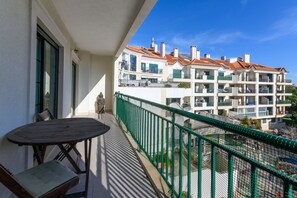 En balkon med et bord og stole, med udsigt over en bygning med flere balkoner og et rødt tegltag.