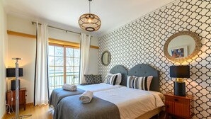A hotel room with two beds, a large window, a patterned wall, and a bedside lamp. - CARCAVELOS BEACH. A wonderful 2 bedroom apartment (Carcavelos)