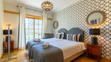 A hotel room with two beds, a large window, a patterned wall, and a bedside lamp.
