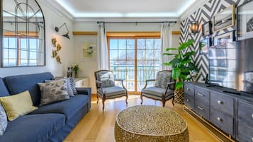 A modern living room with a blue sofa, two armchairs, a round coffee table, and a TV on a dark wooden cabinet.