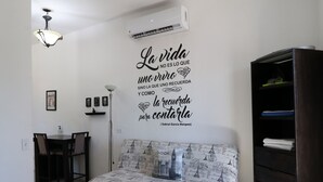 Une chambre à coucher comprenant un lit, un ventilateur de plafond, un climatiseur fixé au mur, un bureau avec des chaises et une bibliothèque.