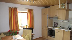 A compact kitchen with a dining area, featuring a table with a vase of flowers, wooden cabinets, and a window with curtains.