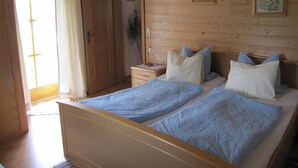 A wooden-paneled bedroom with two beds, a nightstand, a door, and a window with curtains.
