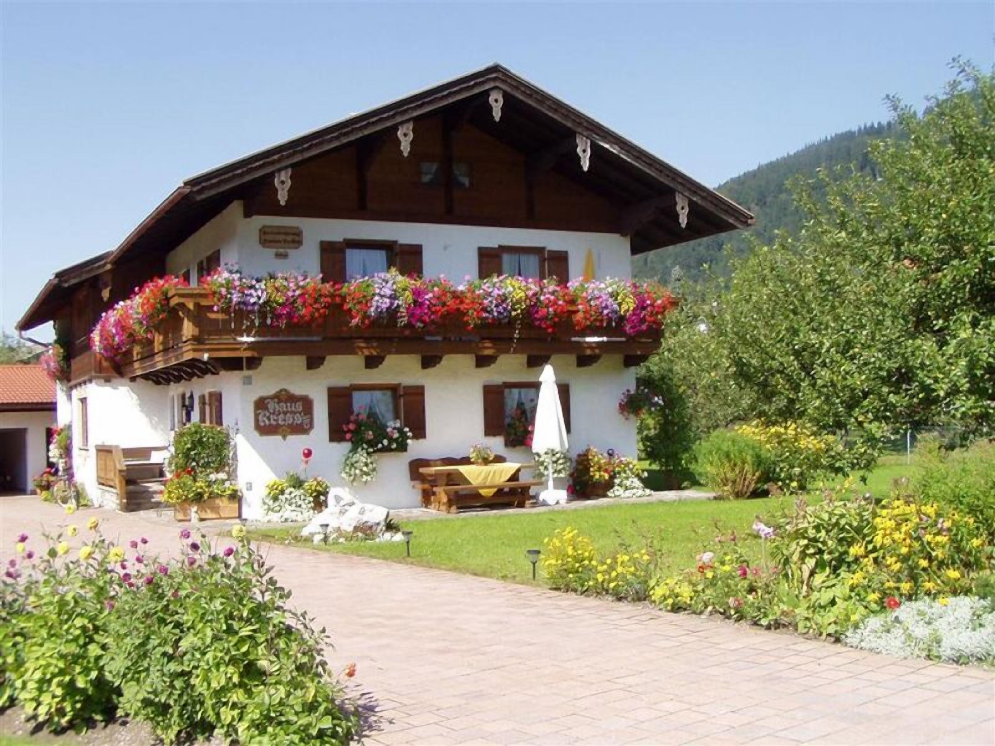 A traditional chalet with a balcony adorned with colorful flowers, a wooden bench outside, and a sign reading "Bar Ristorante".