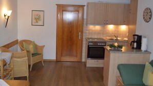 A compact kitchen with wooden cabinets, a built-in oven, a coffee maker, and a clock on the wall.