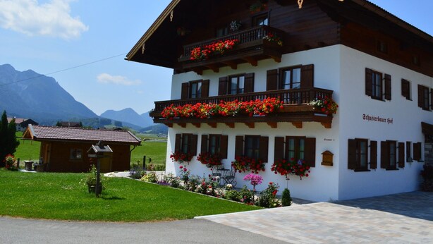 A traditional chalet with balconies adorned with flowers, set against a mountainous backdrop.