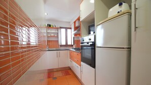 Una cocina con paredes de azulejos naranjas, armarios blancos y un refrigerador de acero inoxidable.