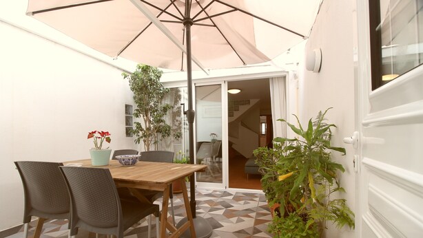 Un patio con mesa y sillas de madera, un paraguas grande y plantas en macetas.