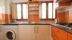 Una cocina compacta con lavadora, un lavamanos y armarios color naranja.