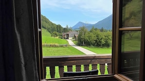 A room with a large window overlooking a green landscape with a path and houses. - C Apartment Röthelmoos Alm 45sqm, balcony and terrace, 1 bedroom, 1 bedsit. (Ruhpolding)