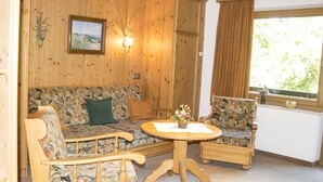 Ein gemütliches Zimmer mit Holzvertäfelung, einer Couch, einem Sessel, einem kleinen Tisch und einem Fenster mit Blick auf Grünflächen.