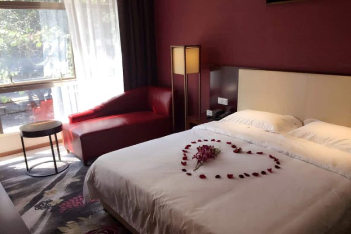 Una habitación de hotel con una cama, un sillón rojo, una mesita de noche y una mesilla auxiliar.