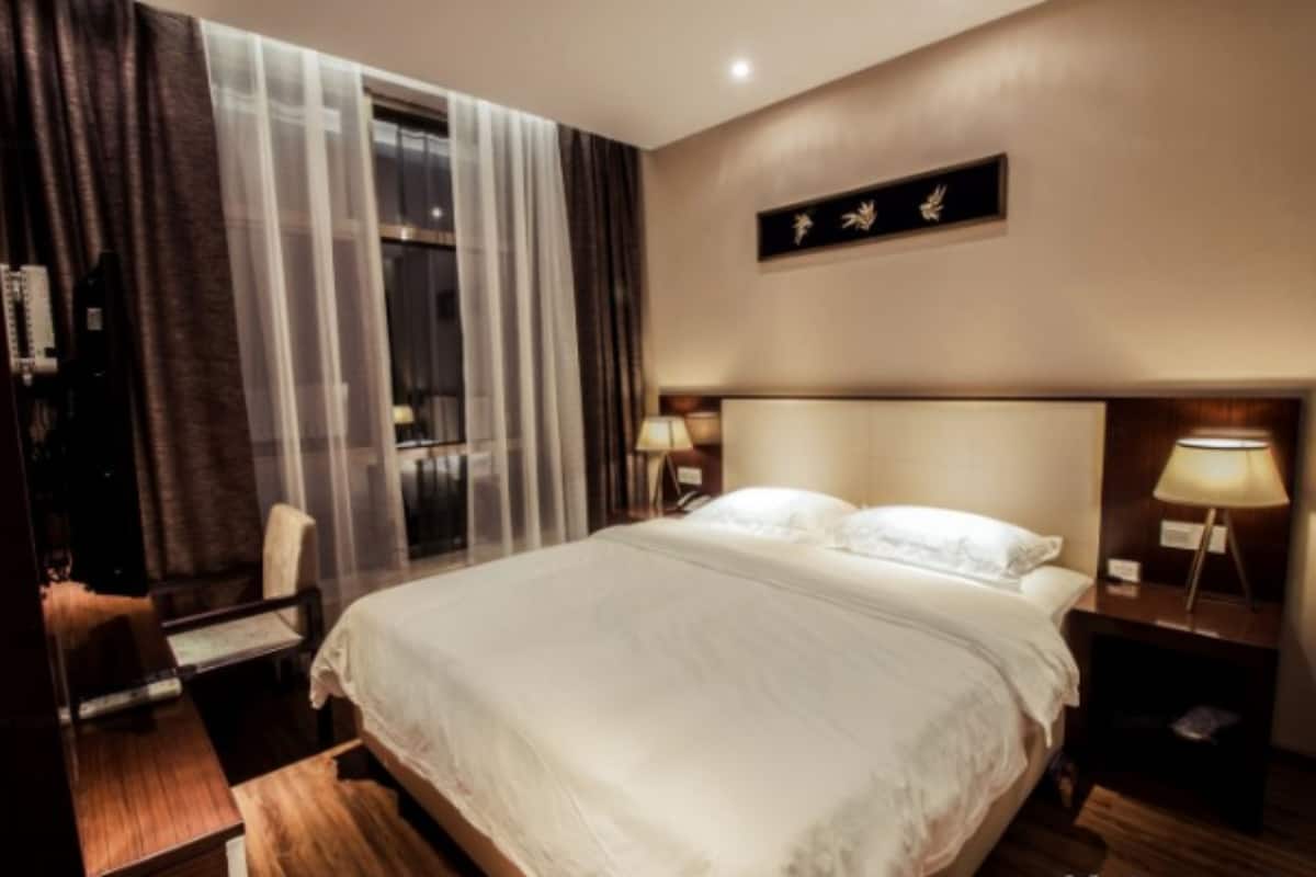 Habitación de hotel con una cama grande, dos lámparas de noche, una mesita de noche de madera, una silla y una ventana con cortinas.
