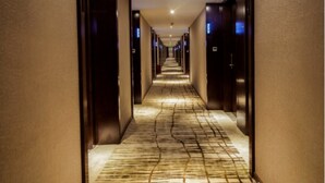 A hotel hallway with a patterned carpet, dark walls, and doors with illuminated signs.