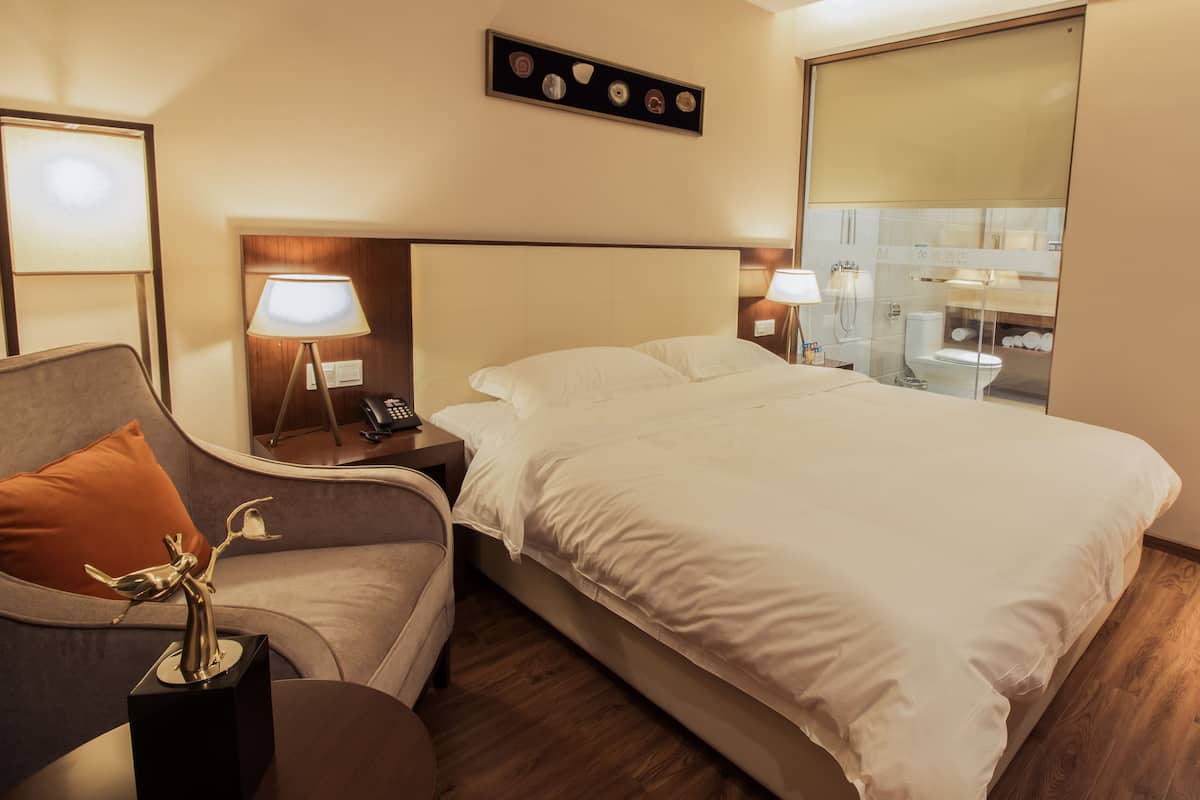 Habitación de hotel con una cama, una mesita de noche con lámpara, un sofá y un adorno sobre la mesita.