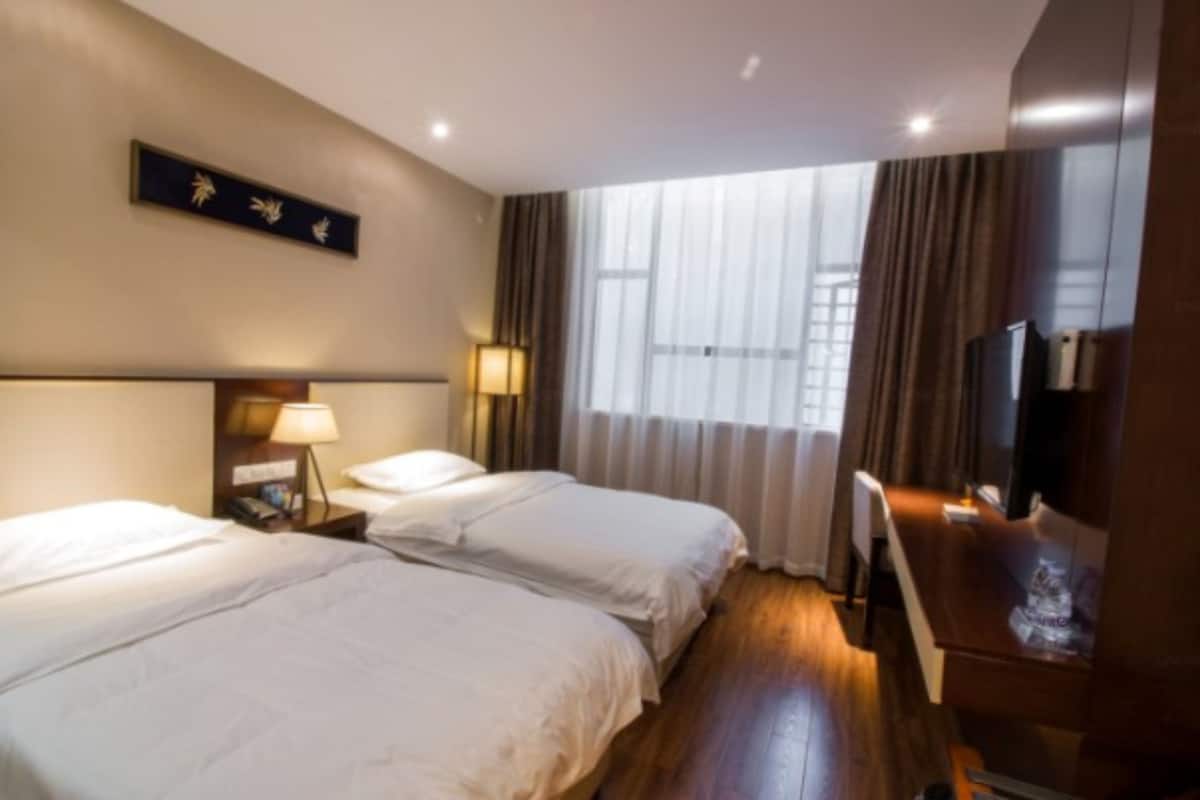 Habitación de hotel con dos camas, televisión y ventana con cortinas.