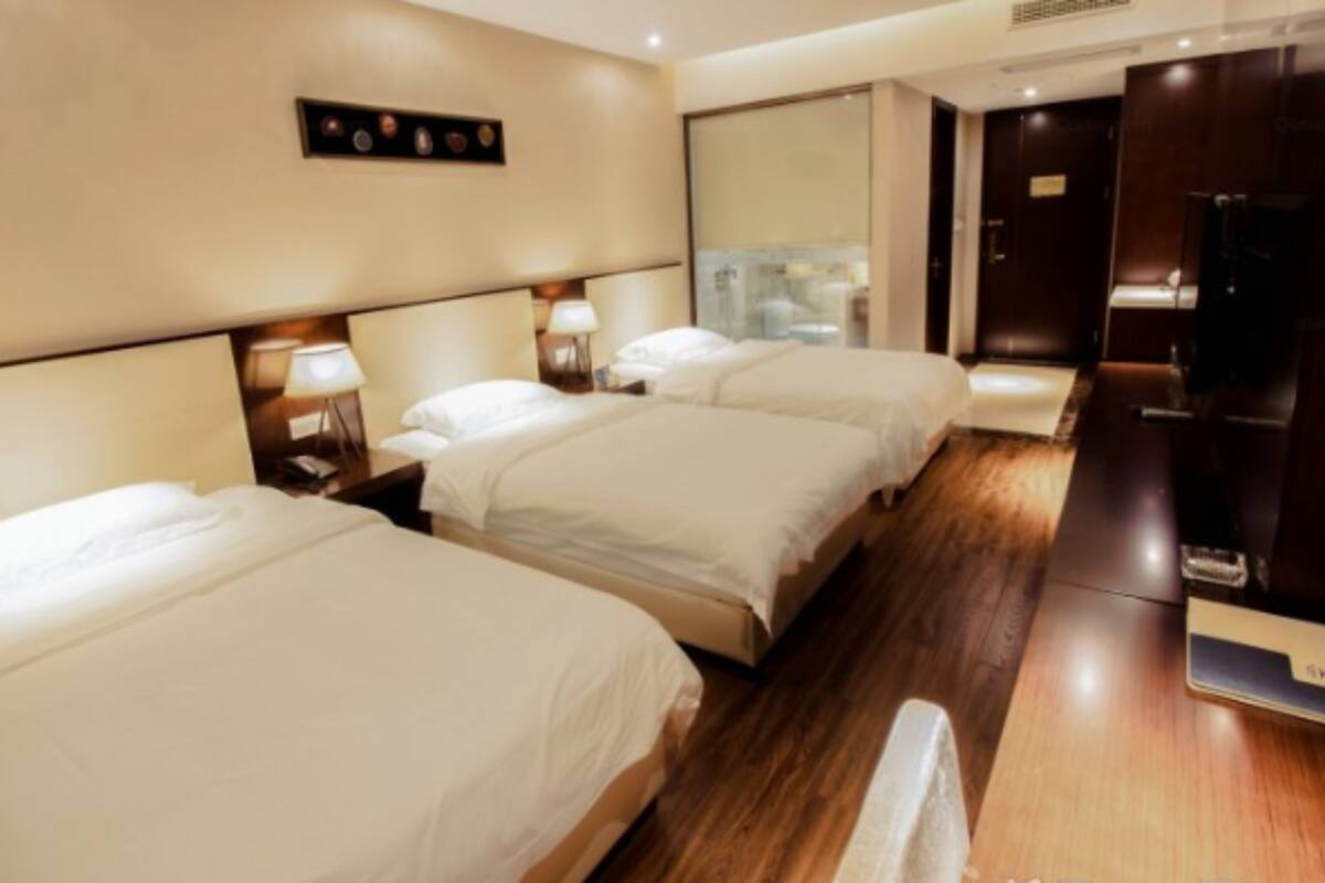 Habitación de hotel con tres camas, suelo de madera y un espejo grande en la pared.